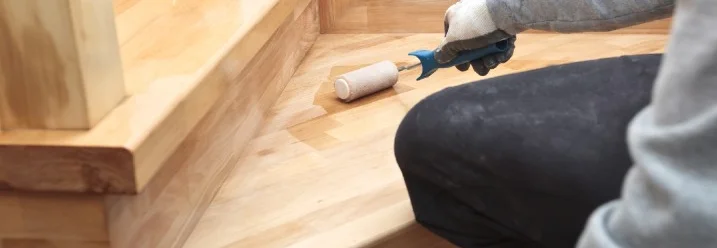 Person ölt Holztreppe mit Farbrolle